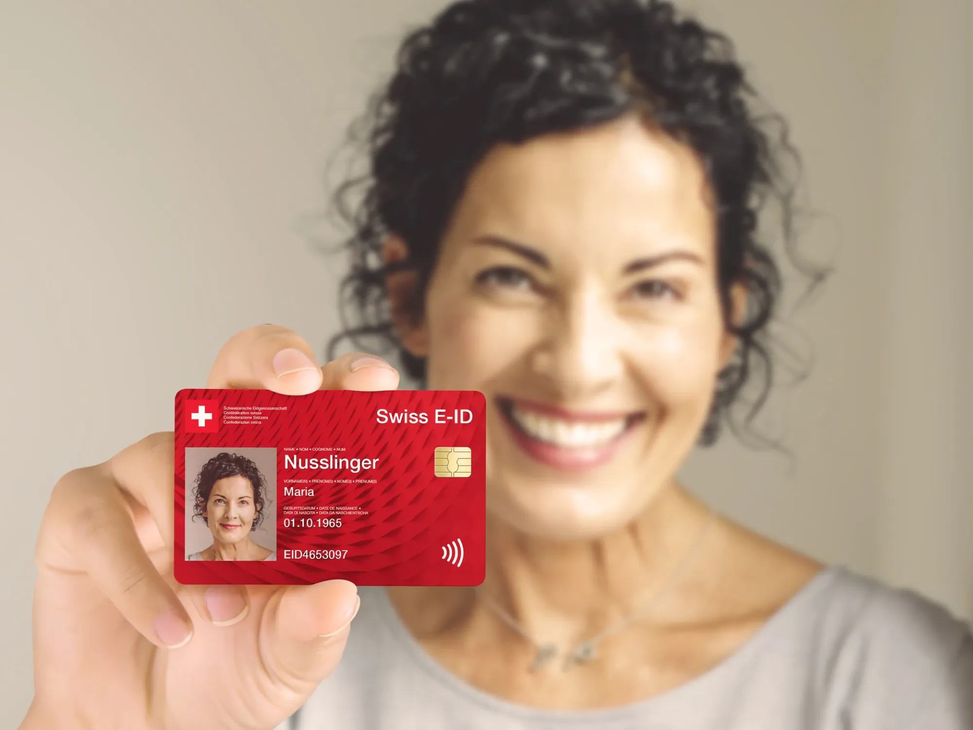 Lächelnde Frau hält eine rote Musterkarte «Swiss E-ID» in die Kamera
