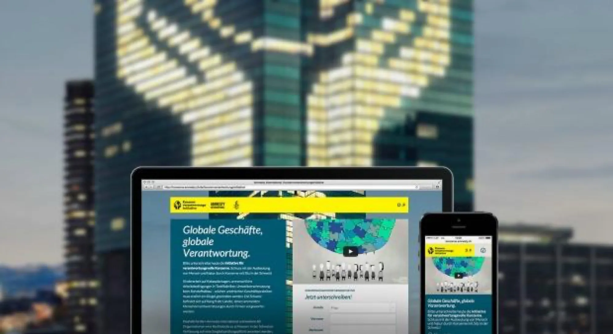 Laptop und Smartphone mit der Kampagnenseite der Konzernverantwortungs-Initiative von 2015, im Hintergrund ein beleuchtetes Hochhaus