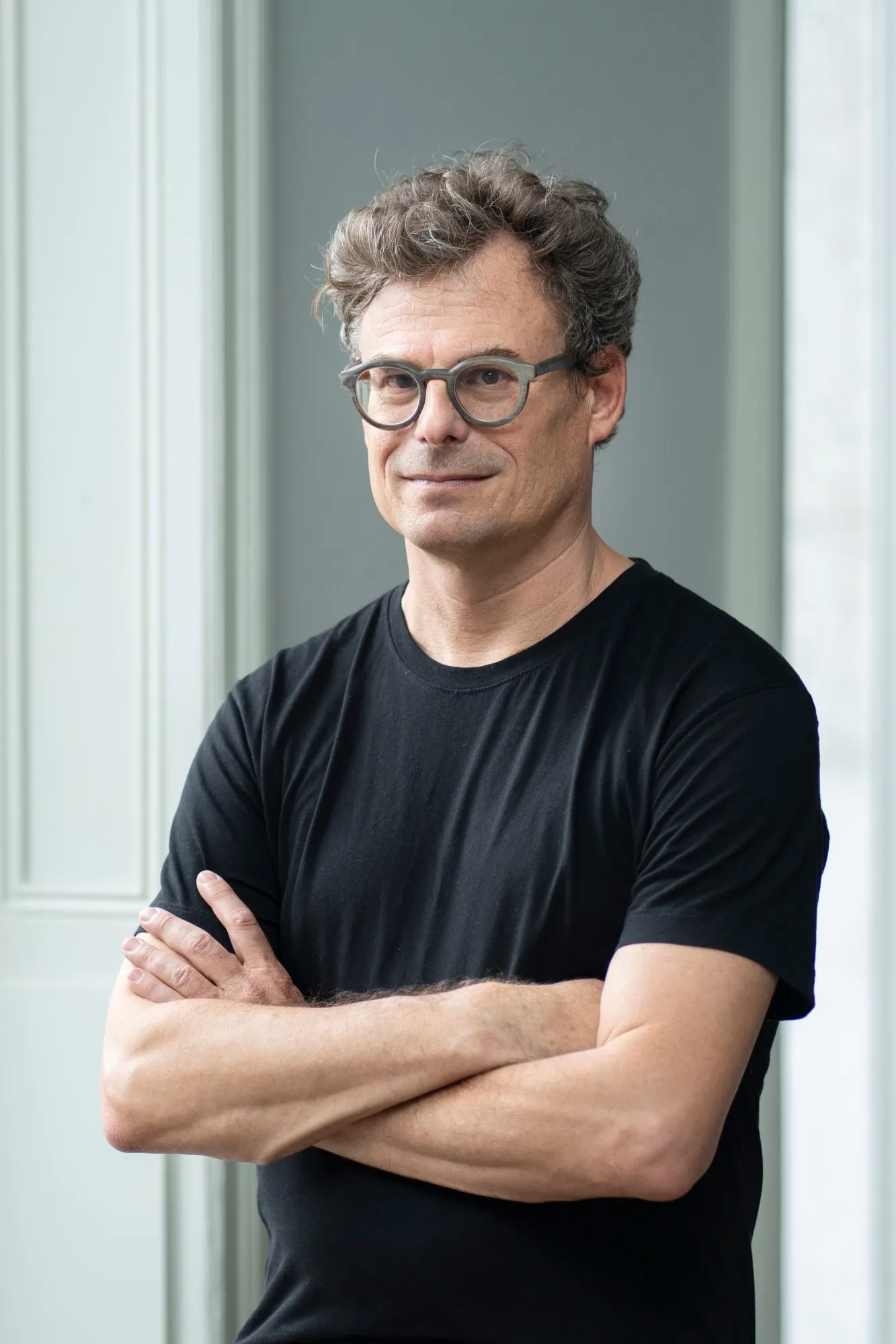 Daniel Graf mit Brille und schwarzem T-Shirt, die Arme verschränkt, vor einer hellen Wand