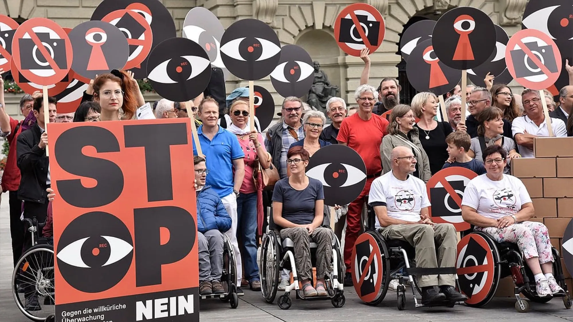 Protestaktion vor dem Bundeshaus: Menschen, einige im Rollstuhl, mit Augen-Schildern und einem Plakat «Stop – Nein»