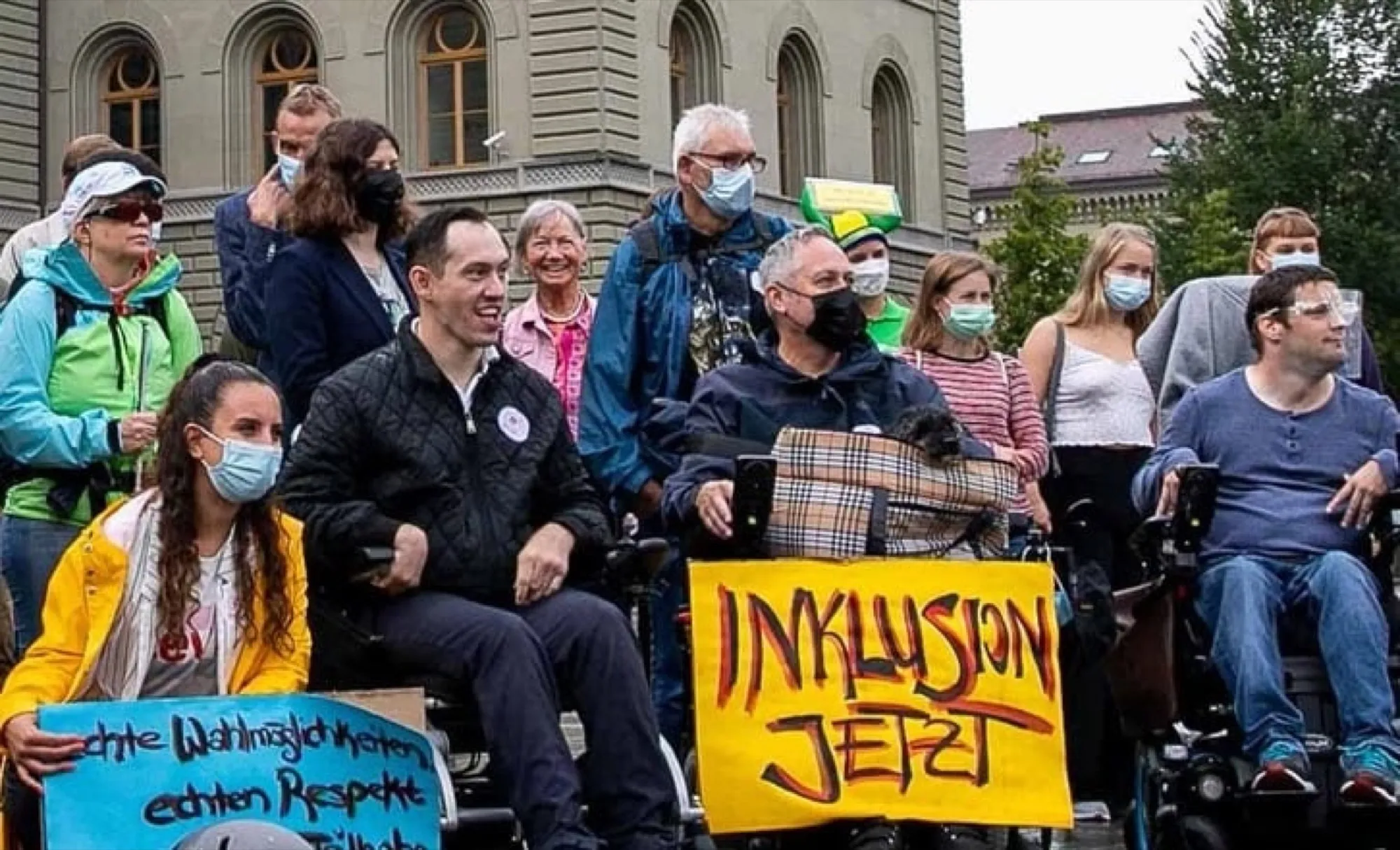 Kleine Gruppe vor dem Bundeshaus, einige im Rollstuhl, mit einem Schild «Inklusion jetzt»